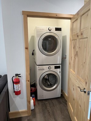 A laundry room with two stacked washing machines, a fire extinguisher, and a wooden door.