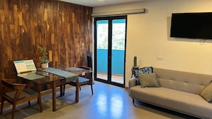 Una sala de estar moderna con una mesa de comedor de vidrio, sillas de madera, un sofá y un televisor montado en la pared.