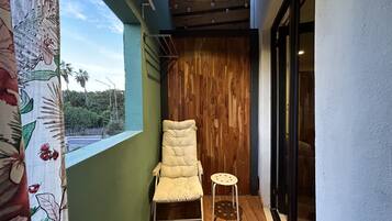 Un balcón con una silla acolchada y un taburete pequeño, suelo de madera, una pared verde y una puerta de madera.