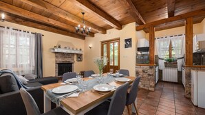 A dining area with a wooden table set for four, surrounded by grey upholstered chairs. A fireplace is visible in the background, and a kitchen area is to the right. - Gorgeous home in Pazin (Pazin)