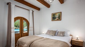 A bedroom with a wooden door leading to a pool, a bed with a white and beige bedspread, and a painting on the wall. - Gorgeous home in Pazin (Pazin)