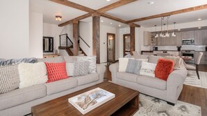 Ein geräumiges Wohnzimmer mit zwei grauen Sofas, Holzbalken, einem Couchtisch aus Holz und einer Küche im Hintergrund.