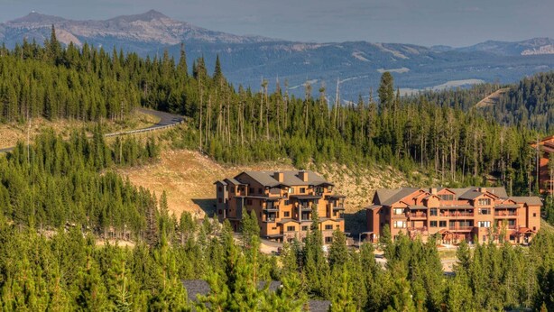 Eine Lodge mit mehreren Gebäuden, umgeben von dichtem Wald und Bergen im Hintergrund.