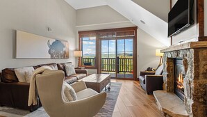 Un salon spacieux avec une cheminée, un grand téléviseur et un balcon offrant une vue panoramique.