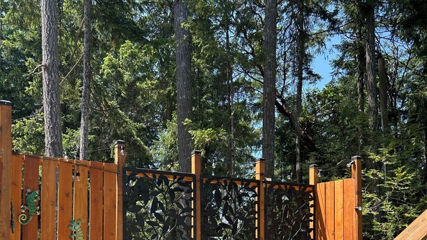 Een houten terras met een metalen hekwerk, een houten trap en een overdekte barbecue.