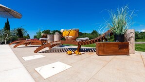 An outdoor seating area with wooden benches, a planter with tall plants, and a clear blue sky.
