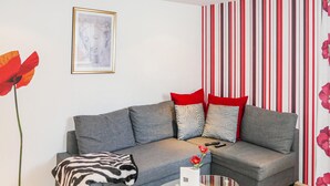 Un salon avec un canapé gris, un papier peint à rayures rouges et blanches, un tableau encadré et un vase rempli de fleurs rouges.