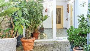 Une cour agrémentée de plantes en pot, dotée d’un sol carrelé et d’une porte donnant sur un espace intérieur.