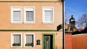Un bâtiment à deux étages, avec trois fenêtres à l’étage supérieur et deux fenêtres à l’étage inférieur, toutes dotées de cadres et de rideaux blancs.