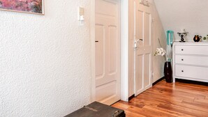 Une pièce avec un plancher en bois, des murs blancs, une commode blanche et une porte dotée d’un interrupteur.