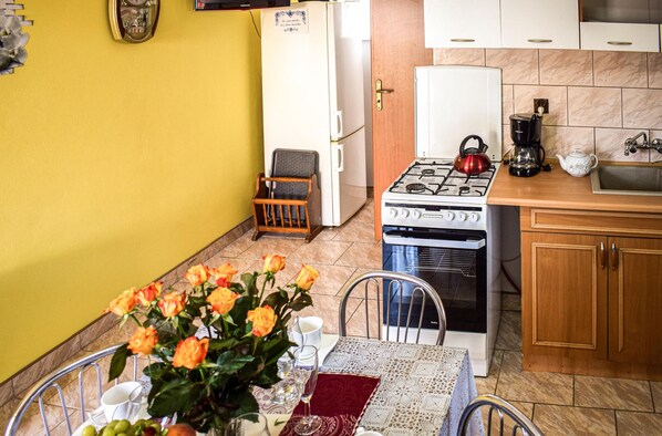 Une cuisine compacte équipée d’une cuisinière à gaz, d’un four et d’un réfrigérateur. On y trouve une table à manger agrémentée d’un vase de fleurs et d’un chemin de table rouge.