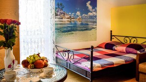 Un dormitorio con una cama, una mesa con frutero, un florero con flores y un cuadro de una playa.