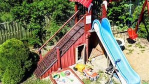 Un parque infantil con un tobogán, columpios y un pequeño edificio rojo.