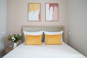 Ett hotellrum med en säng, två kuddar, ett nattduksbord, en lampa och en vas med blommor.
