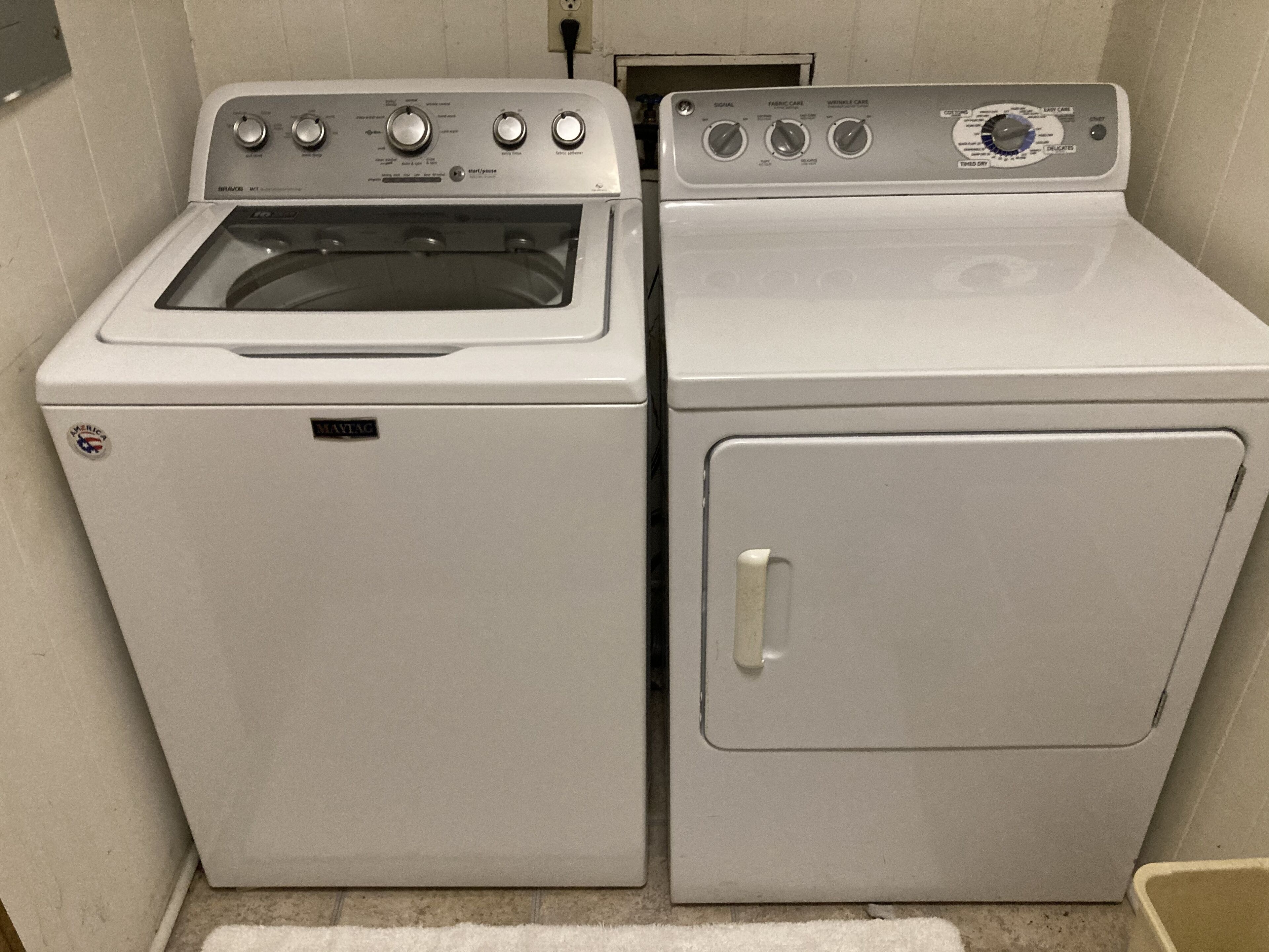 Ein kleiner Waschraum mit einer Waschmaschine und einem Trockner mit Frontlader, inklusive Bedienelementen und einem sichtbaren Stromkabel.