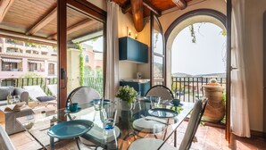 A dining area with a glass table and chairs, a view of the cityscape, and a balcony with a potted plant. - Rokkaria by Interhome (Villasimius)