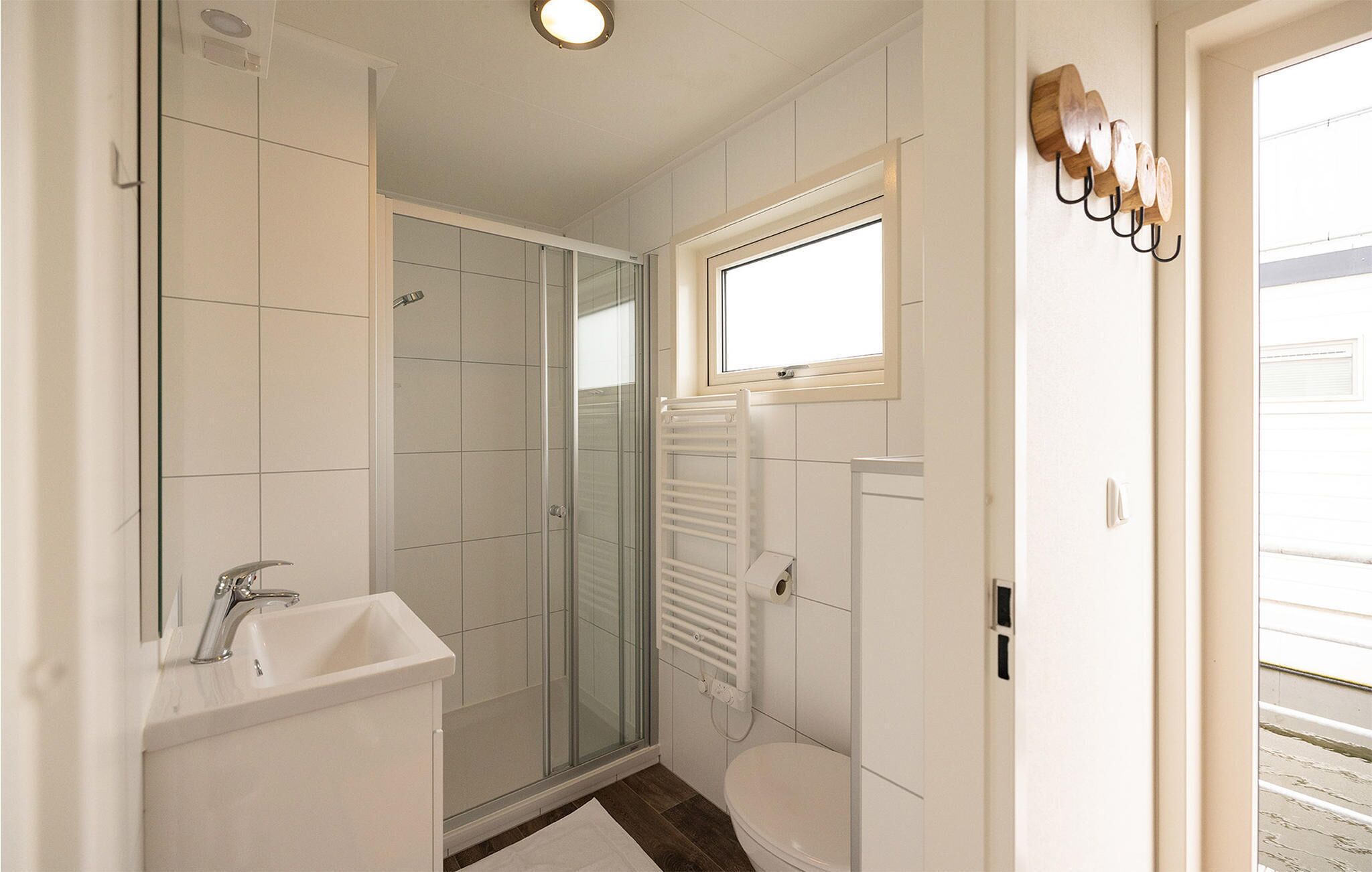 Een badkamer met een douche, wastafel, toilet en een raam.