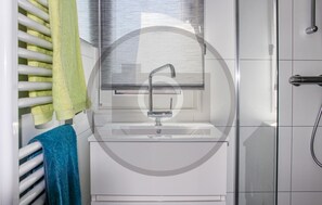 A bathroom with a white sink, a towel rack with a green towel, and a shower area. - Cozy ship in Ohé & Laak with WiFi (Ohé & Laak)