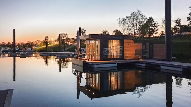 A modern building with a glass facade, situated by a calm body of water, likely a marina.