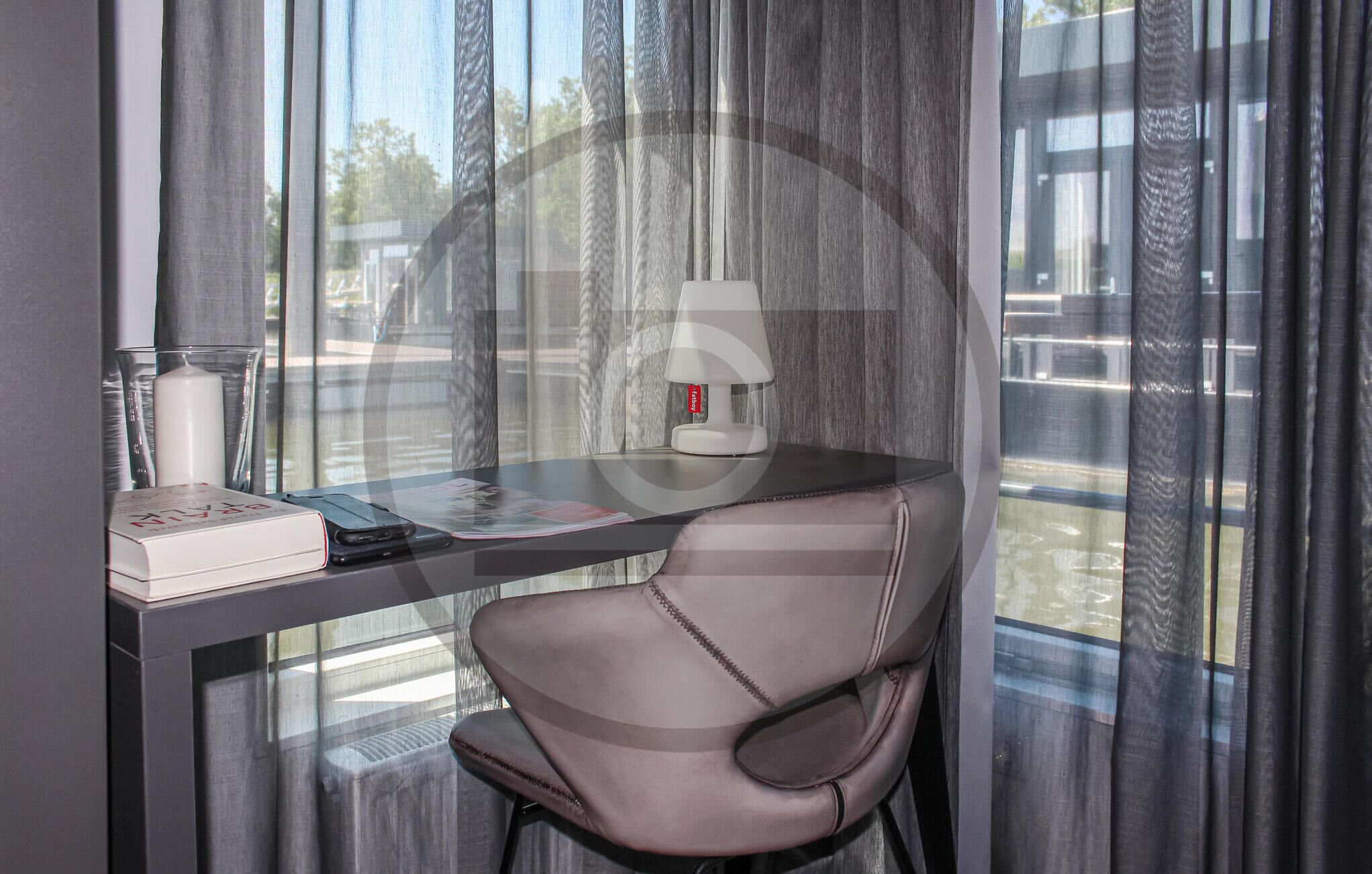 A modern hotel room with a glass desk, a laptop, a lamp, and a chair.