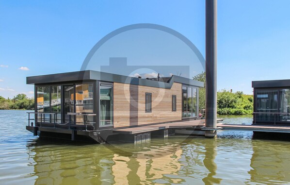 A modern floating house with large windows, a deck, and a water body in the background. - Cozy ship in Ohé & Laak with WiFi (Ohé & Laak)