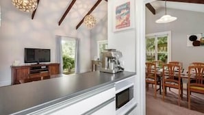 Cozinha moderna com uma ilha grande, área de jantar com cadeiras de madeira e televisão na parede.