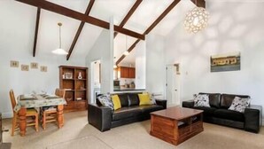 Uma sala de estar ampla com um sofá preto, uma mesa de centro de madeira e uma área de refeições com mesa e cadeiras.