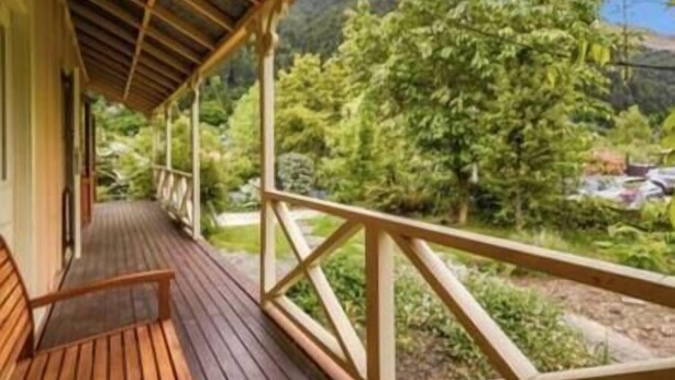 Um deck de madeira com guarda-corpo, com vista para uma paisagem verde exuberante com árvores e céu claro.