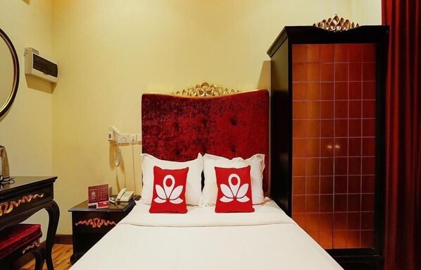A hotel room with a red upholstered headboard, a white bedspread, and two red pillows with a white design. There is a wooden nightstand with a telephone and a small table with a red object on it. A mirror is on the wall, and a red curtain is partially visible. - Hotel 1888 Collection (Singapore)