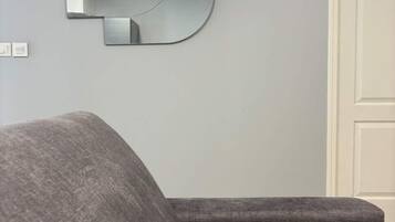 Un salón moderno con un sofá gris, un espejo montado en la pared y una puerta cerrada.