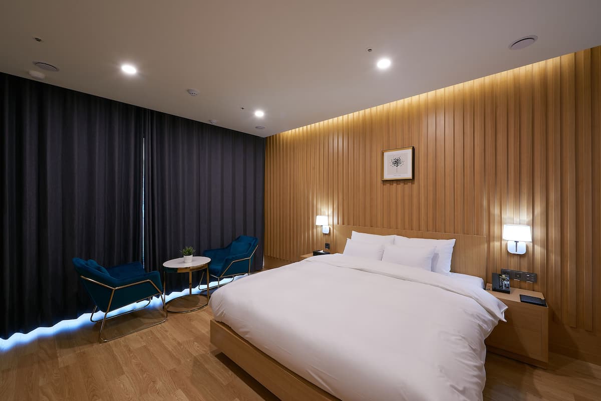 Una habitación de hotel moderna con una cama grande, dos sillas, una mesita y un panel de pared de madera.
