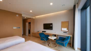 Habitación de hotel con dos camas, un escritorio con silla, un televisor y un ventanal grande.