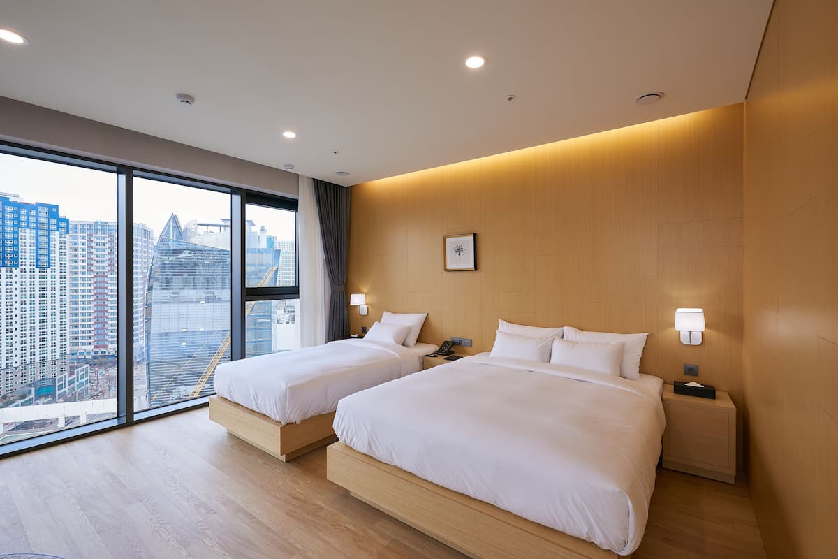 Una habitación de hotel moderna con dos camas, ventanas amplias y vistas a la ciudad.