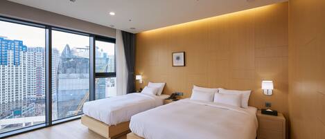 A modern hotel room with two beds, large windows, and a city view.