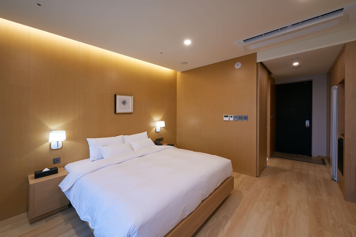 Una habitación de hotel con una cama grande, lámparas de noche, una mesita de noche y un cuadro colgado en la pared.