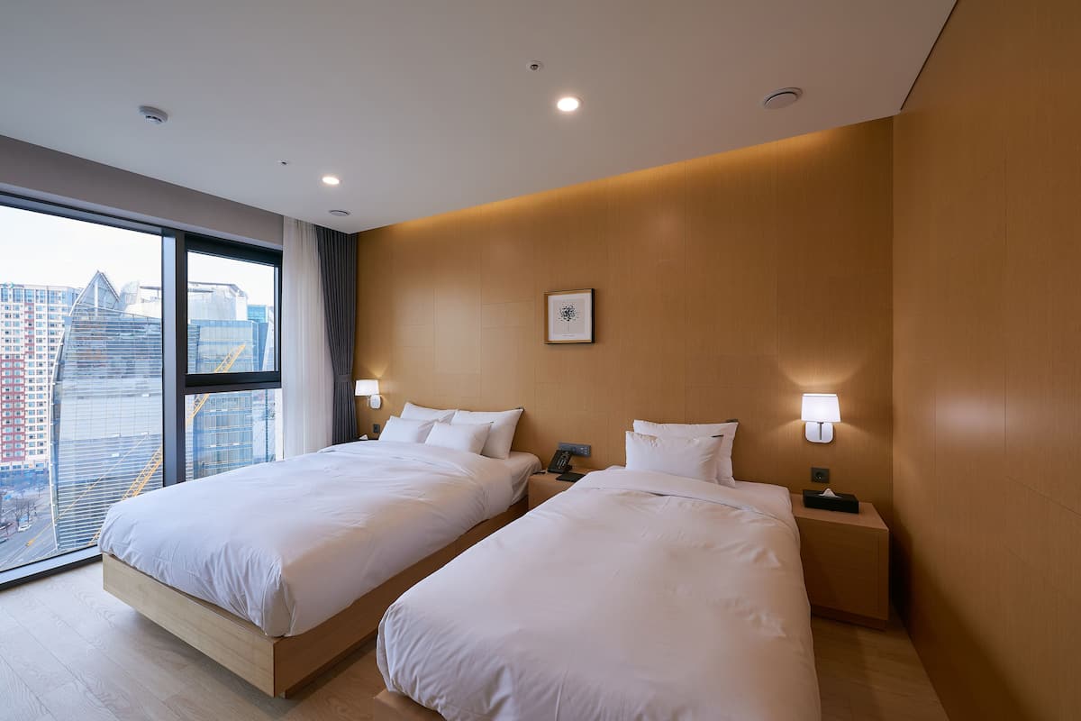 Habitación de hotel con dos camas, un ventanal con vista a la ciudad y una pared de acento de madera.