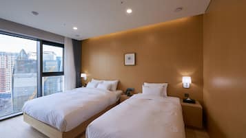 A hotel room with two beds, a large window with a city view, and a wooden accent wall.