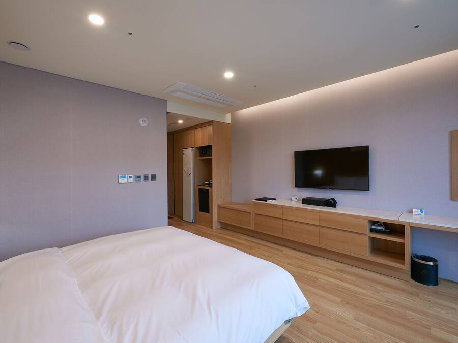 Una habitación de hotel con cama, escritorio, televisor y una kitchenette pequeña.