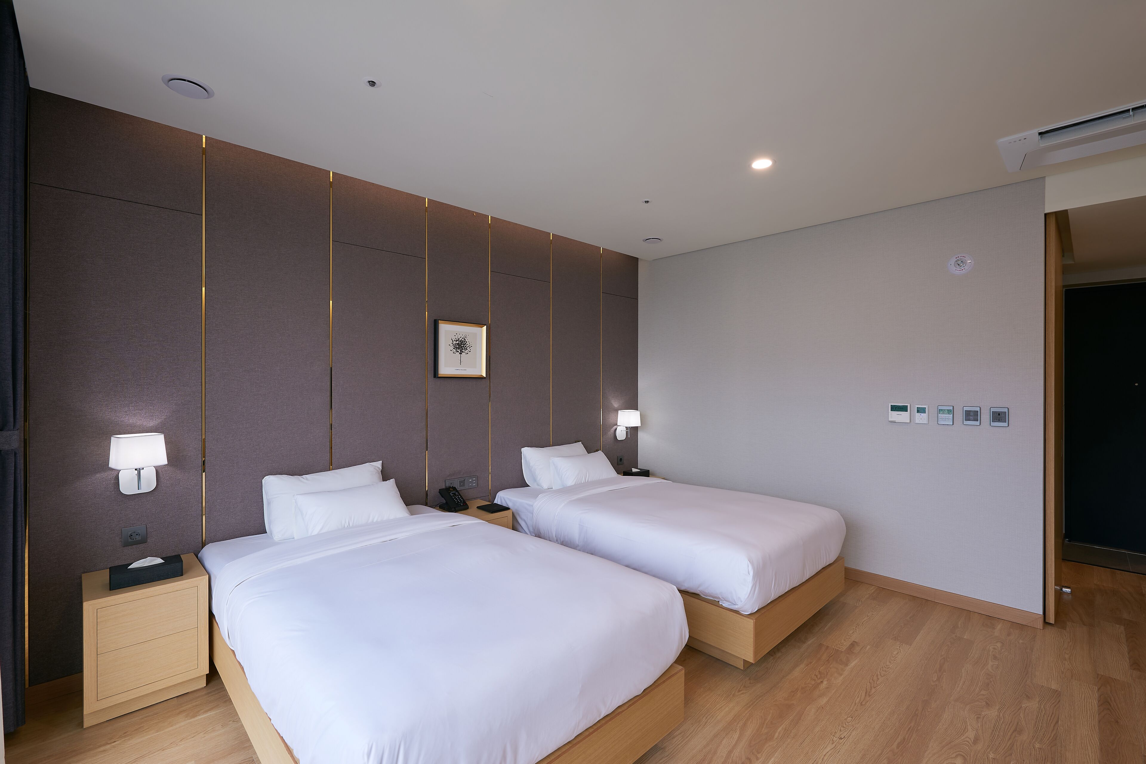 A hotel room with two beds, bedside tables, lamps, a wall-mounted phone, and a picture.