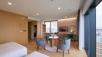 A hotel room with a bed, a round table with chairs, a desk with a chair, a TV, and a large window.