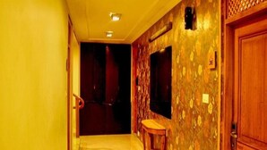A hallway with a wooden door, a small table, and a wall-mounted television. - Pine Spring Hotel (Anantnag)