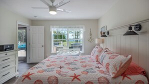 Un dormitorio con cama, ventilador de techo, ventana con vistas, escritorio y silla.
