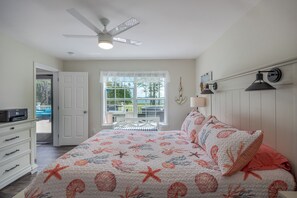 Un dormitorio con cama, ventilador de techo, ventana con vistas, escritorio y silla.