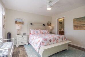 Une chambre à coucher avec un lit, des tables de chevet, un ventilateur de plafond et des œuvres d’art accrochées aux murs.