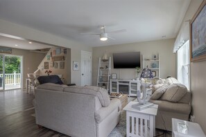 Un salón con un sofá gris, una mesa de centro blanca y un televisor montado en la pared.