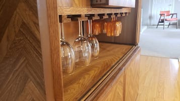 Un área de bar con barra de madera, un estante con copas y botellas de vino.