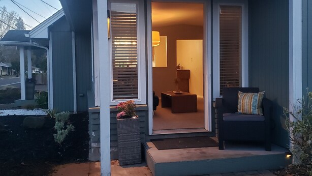 A house with a covered porch, a seating area with a sofa and armchair, and a small table.