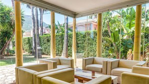 A sunlit indoor seating area with large windows, a stone floor, and a view of a lush garden and distant buildings. - Cozy home in Dénia with private swimming pool, can be inside or outside (Dénia)