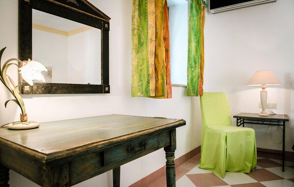 Una habitación con una mesa de madera, una silla verde, un espejo y una lámpara.