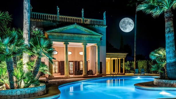 A poolside view of a hotel with a classical facade, a moon in the sky, and palm trees. - Cozy home in Dénia with private swimming pool, can be inside or outside (Dénia)